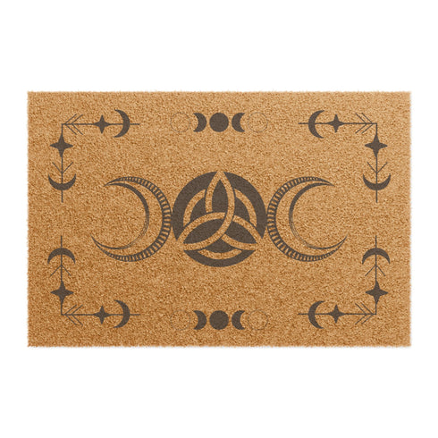 Rectangular coir doormat with central triple moon and triquetra symbol, surrounded by celestial motifs including stars and moon phases, in dark brown on natural tan background.